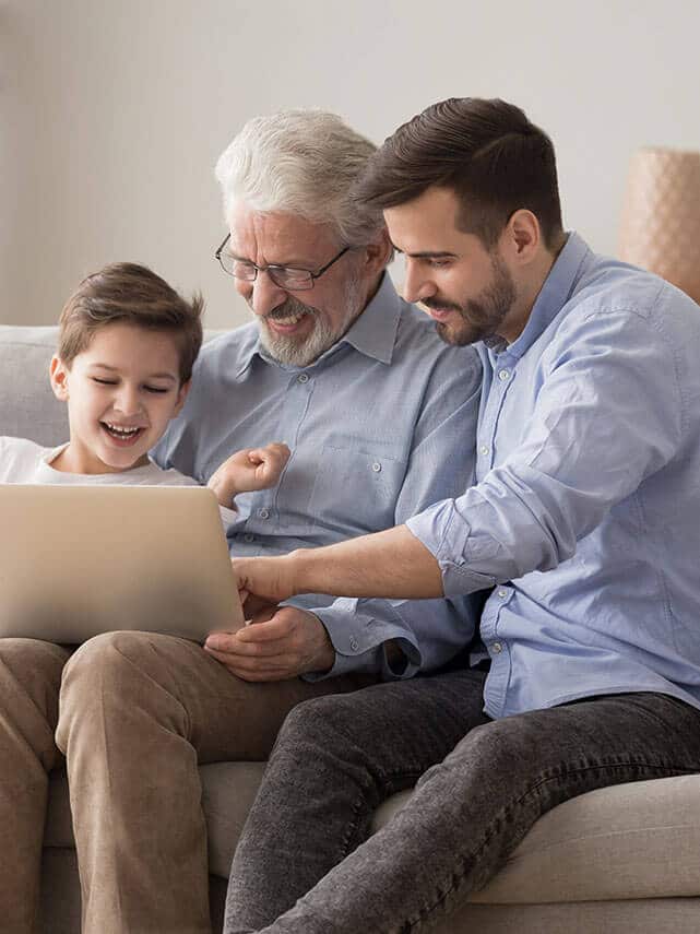 Grandfather, father and son smile while watching something in a laptop.