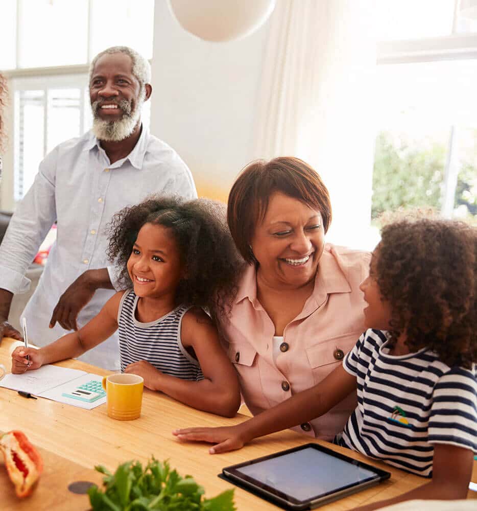 Grandmother, grandfather, and two child grandkids smile while making homework at a table
